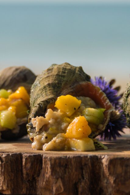 Guscio di rapana venosa farcito con del cibo e posta su un tagliere di legno