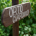 Cartello in legno in mezzo alle piante indica la direzione dell'orto e del giardino