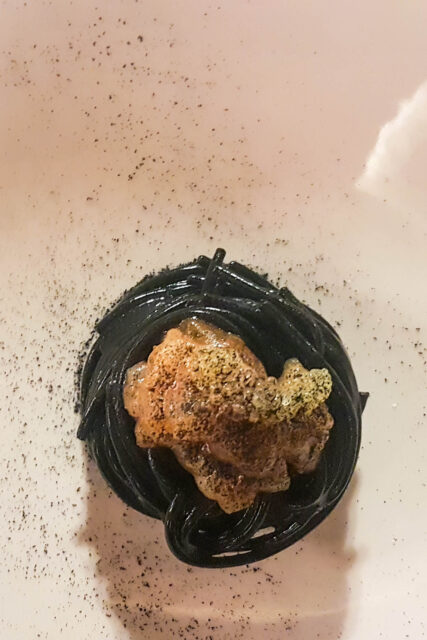Dentro a un piatto bianco un nido di spaghetti neri con sopra tartare di gamberi viola