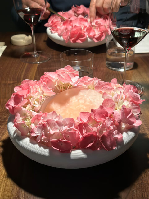 Un piatto con al centro la pietanza e circondato da fiori rosa