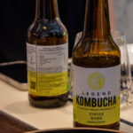 Una bottiglia di Legen Kombucha su una tavola con un piatto sfuocato davanti