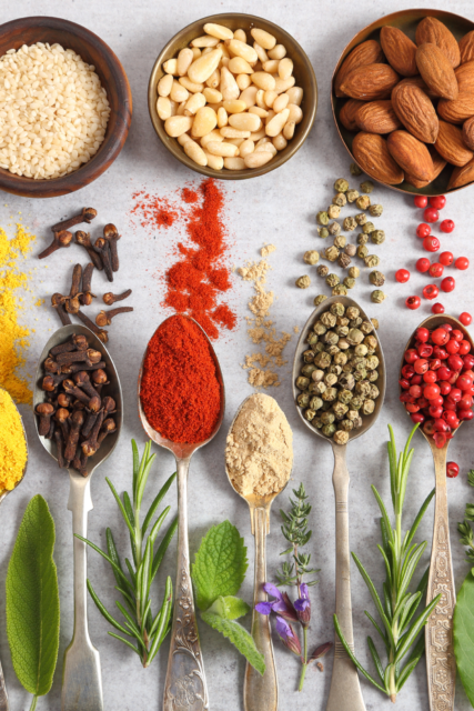 Rametti di erbe aromatiche, cucchiaini pieni di spezie e ciotole con frutta secca